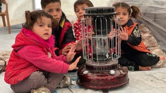 Barn på flykt från Syrien värmer händerna över en kamin i ett tältläger i Irak.