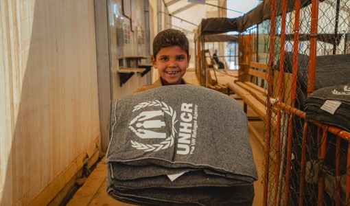 En pojke tittar in i kameran. Han har grå filtar i sin famn.