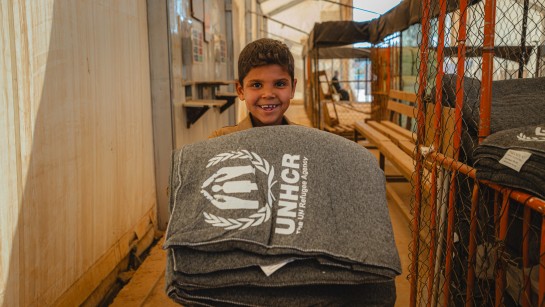 En pojke tittar in i kameran. Han har grå filtar i sin famn.