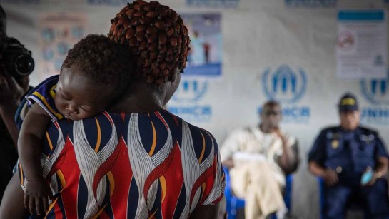En kvinna håller sitt barn över axeln, hon väntar på humanitär hjälp i ett av UNHCR mottagningscenter.