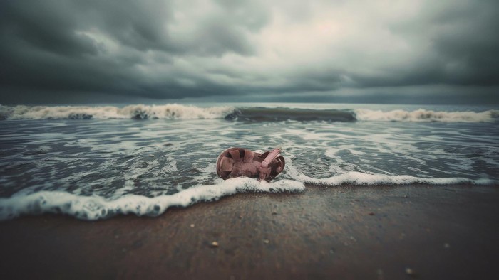 En liten plastsandel ligger och skumpar på en strandkant med havet bakom sig.